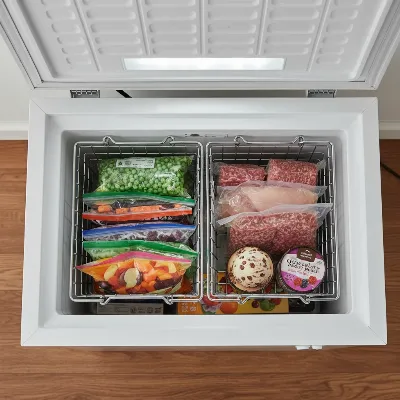 The interior of a small chest freezer, neatly organized with various frozen foods in removable baskets.